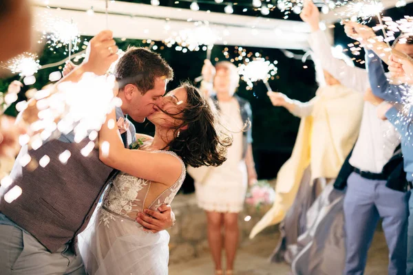 Vőlegény és menyasszony csók a vendégek között csillagszórókkal az esküvői partin — Stock Fotó