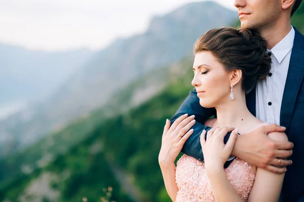 Marié debout sur la montagne - le marié étreint doucement la mariée par derrière — Photo