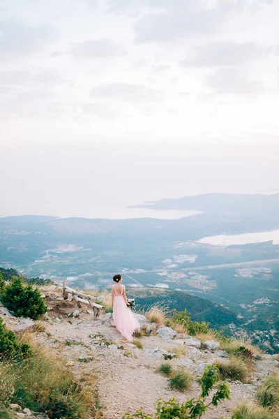 Mooie bruid en staan op de berg, vasthouden van boeket en kijken naar de baai van Kotor — Stockfoto