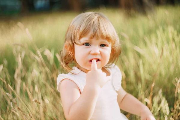 Liten flicka sitter utomhus och håller ett finger i munnen — Stockfoto