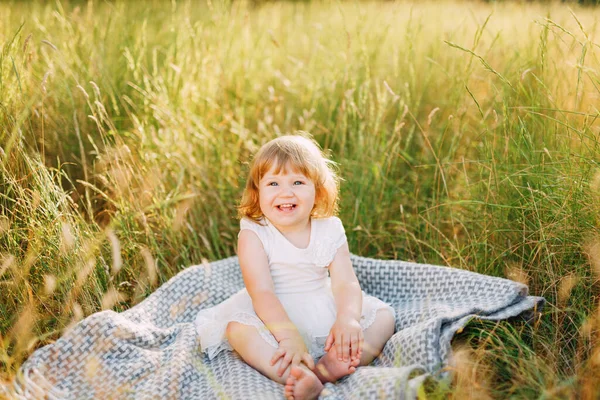 Niña se sienta en una alfombra al aire libre y sonríe —  Fotos de Stock