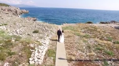 Gelin ve damat el ele tutuşun ve Lustica 'daki kayalık plaja doğru yürüyün.