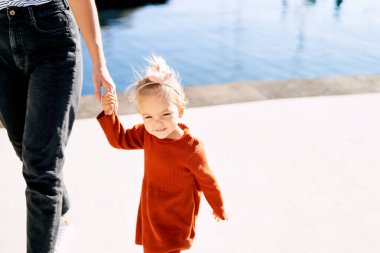 2 yaşında tatlı bir kız deniz kenarında yürürken annesinin elini tutuyor.