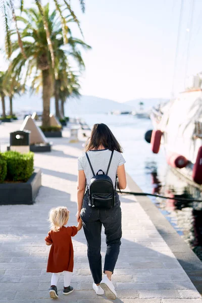 Mother and daughter are walking hand in hand on a boat pier in Porto Montenegro