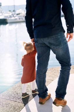 Baba ve kızı güneşli bir günde el ele yürüyorlar.