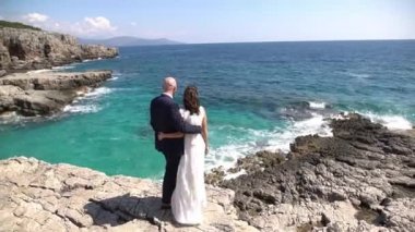 Gelin ve damat kayalık bir sahilde sarılıp ufka bakıyorlar.