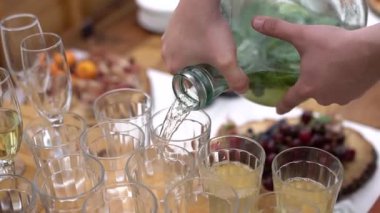 Düğün yemeği dışarıda, erkekler bardaklara içki doldurur.