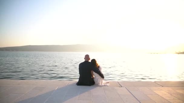 Der Bräutigam und die Braut sitzen umarmt auf dem Steg in Porto Montenegro, die Braut ruhte ihren Kopf auf der Schulter des Bräutigams — Stockvideo