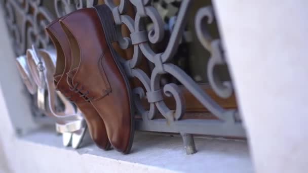 Los zapatos de los novios y las sandalias de las novias están cerca de la grácil red de hierro forjado — Vídeo de stock