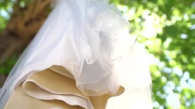 Güneşli bir günde bir ağacın yeşil dallarında sallanan havadar bir şifon etekli narin nedime elbisesinin alt görüntüsü.