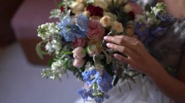 Gelin elinde bir buket tutuyor ve parmaklarıyla çiçeklere dokunuyor.