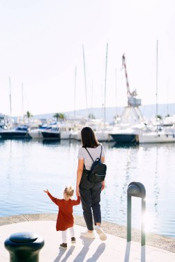 Küçük kız annesiyle birlikte teknelere bakıyor.