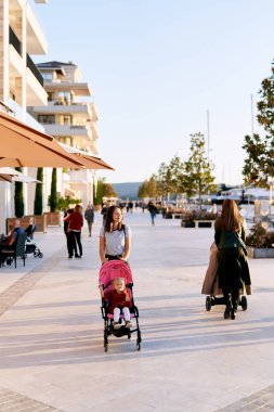 Anne, Porto Karadağ 'da bir tekne iskelesinde yürürken çocuğunu pembe bir pusete itiyor.