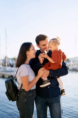 Ebeveynler kızlarına gülümsüyor. Kızları beyaz bir zakkum çiçeğine bakıyor.