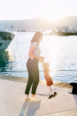 Anne gün batımında kızını bir tekne iskelesinde döndürüyor.