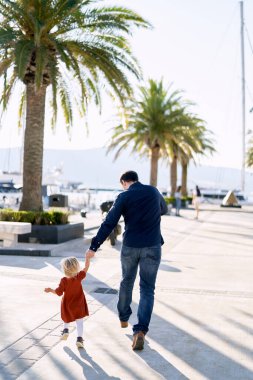 Adam, Karadağ 'da bir tekne iskelesinde yürümekte olan çocuğuyla el ele koşuyor.