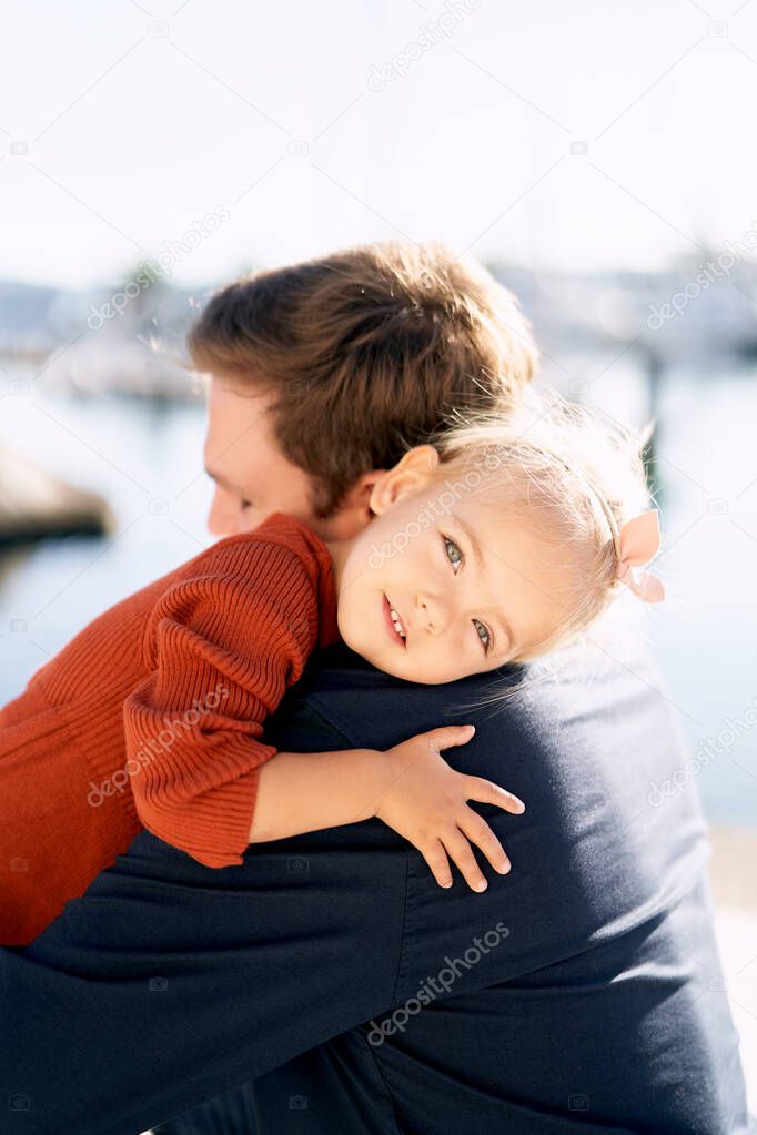 A portrait of a sweet girl hugging her father by the sea