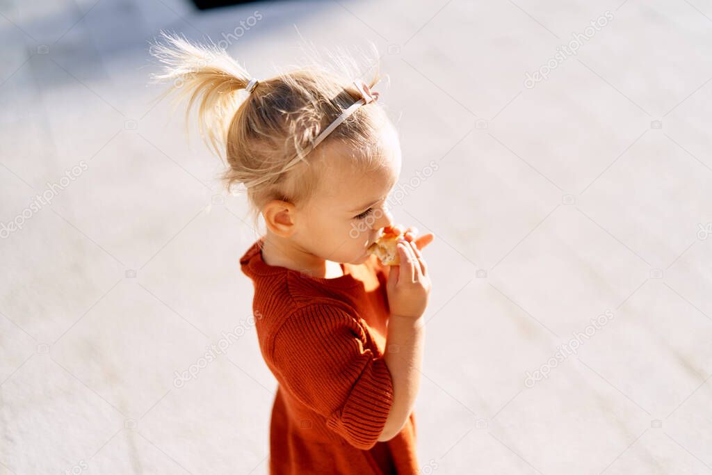 A pretty little girl with a pink bow in her hair is eating a pie on a sunny day