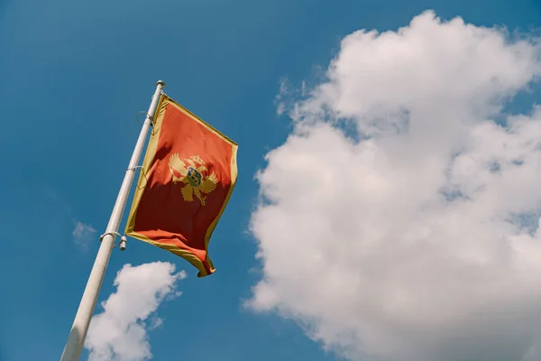 Close-up of the red flag of Montenegro with a two-headed eagle against a blue sky with white clouds. — Stock Photo, Image