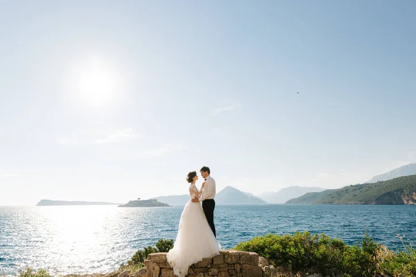 Bride and groom are hugging on the beach of the Mamula island against the backdrop of the Arza fortress — Stock Photo, Image