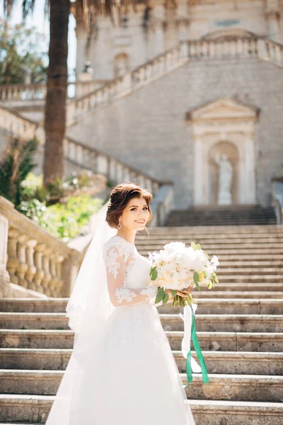 Vacker brud i anbud bröllop klänning med brudbukett på trappan till födelse av den välsignade Jungfru Maria kyrkan i Prcanj — Stockfoto
