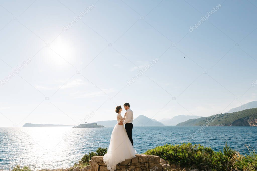 bride and groom are hugging on the beach of the Mamula island against the backdrop of the Arza fortress