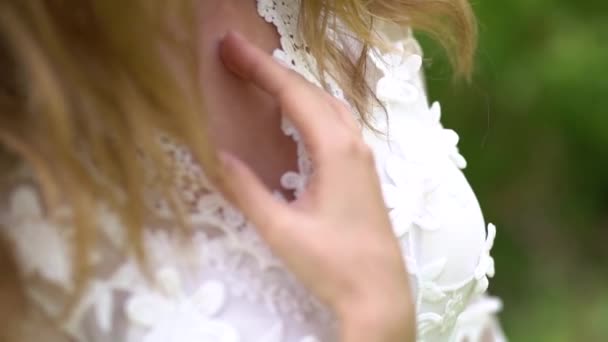 De bruid in een kanten jurk houdt sierlijk haar hand op haar borst — Stockvideo