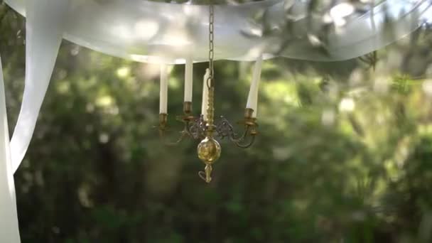 Candelabro y lienzos blancos de tela aireada sobre ramas de olivo en el bosque, decoraciones de bodas — Vídeos de Stock