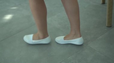 Kadın gelinliğin yanına gelir ve onu askıdan çıkarmak için parmak uçlarında durur.