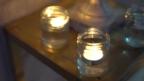 Velas en frascos de vidrio se queman en un soporte de madera de decoración por la noche, primer plano — Vídeos de Stock