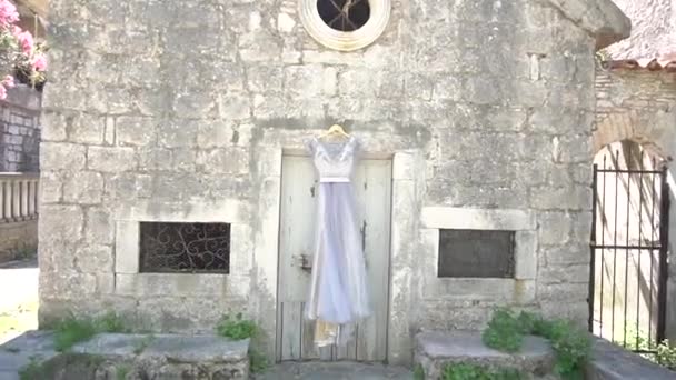 Delicado vestido de dama de honor colgando por encima de la puerta de un edificio de ladrillo viejo — Vídeos de Stock