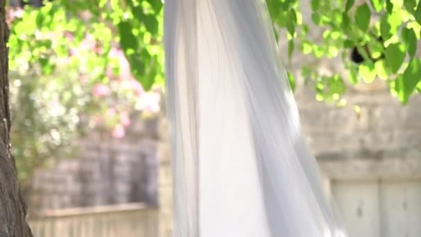Delicado vestido de dama de honra com um corpete bordado com contas e um cinto de cetim pendurado nos ramos verdes de uma árvore em um dia ensolarado — Vídeo de Stock