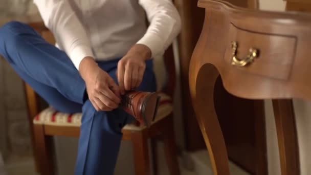 Un hombre se sienta en una silla y ata los cordones en sus zapatos — Vídeos de Stock