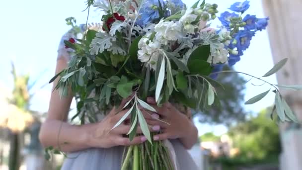 La novia sostiene un ramo en sus manos y se para al aire libre — Vídeo de stock