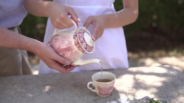 Porselen çaydanlığı tutan ve fincana çay döken çift.