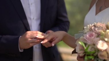 Damat gelinin parmağına yüzük takar, gelin elinde buket tutar.