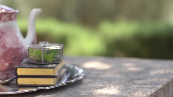 Teekanne und Tasse aus Porzellan, Bücher mit goldenem Vorderrand, Glasschmuckschatulle und Trauringe auf dem glänzenden Tablett — Stockvideo