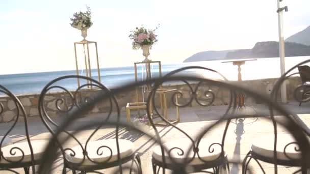 Decoración del lugar de la boda con stands, colgantes de vidrio, jarrones con flores y elegantes sillas de hierro forjado — Vídeos de Stock