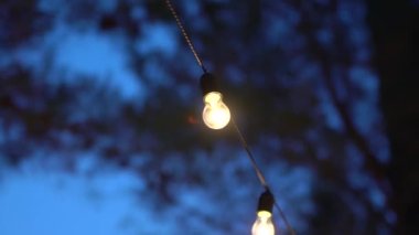 Açık havada parıldayan dekoratif ampullerden oluşan bir çelenk, yakın plan.