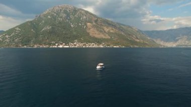 Bir turist teknesi Kotor Körfezi 'nin ortasında yelken açar. Önünde bir dağ ve rahat bir kasaba vardır.