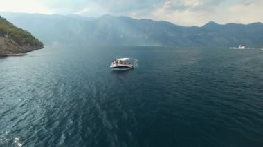 Bir turist teknesi Kotor Körfezi 'nin ortasında yelken açıyor. Önünde bir yelkenli yatı var.