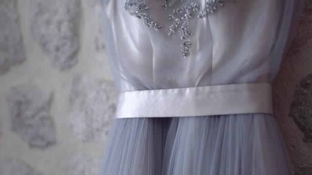 Delicate bridesmaid dress with a bodice embroidered with beads and a satin belt hanging on the wall with decorative stone, close-up — Stock Video