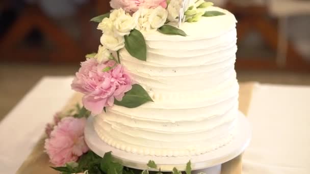Beyaz kremalı düğün pastası, şakayık çiçekleri ve lisianthus ile süslenmiş. — Stok video