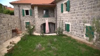 Güzel, soluk, pembe bir gelinlik girişte asılı taş bir duvarda, rahat bir avluda.