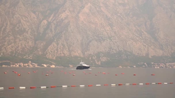 Um iate navega no meio da Baía de Kotor, na frente dele é um monte perto da cidade aconchegante — Vídeo de Stock