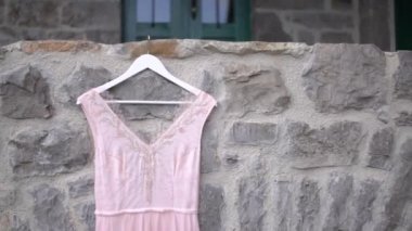 Taş duvarda asılı soluk pembe bir gelinliğin boncuklu korsesi, yakın plan.