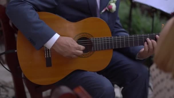 Een man in een pak met een boutonniere speelt akoestische gitaar — Stockvideo