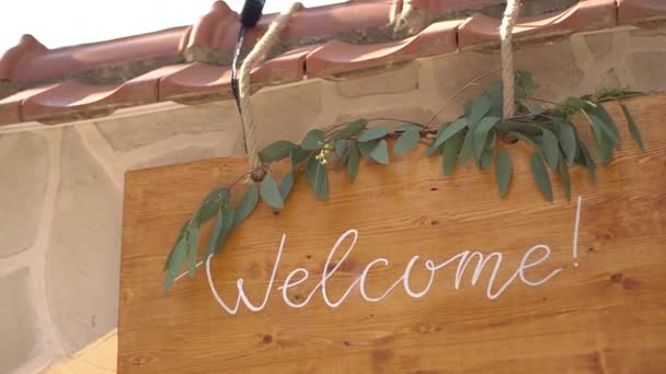 Деревянный стол с надписью Добро пожаловать, украшенный эвкалиптовыми ветвями — стоковое видео