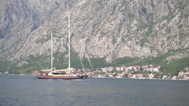 Yelkenli yat Kotor Körfezi boyunca ilerliyor. Arkasında güzel dağlar ve küçük şirin bir kasaba var.
