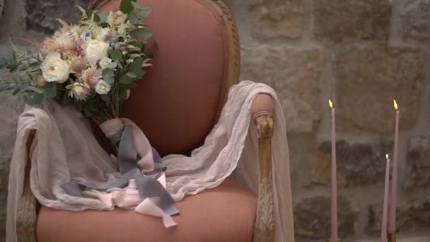 Delicate bridal bouquet and delicate fabric in a pink armchair against a stone wall — Stock Video